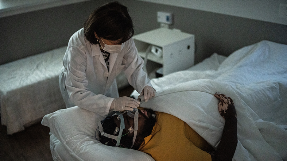 Female doctor in lab coat adjusting breathing apparatus on sleeping patient undergoing a sleep study.